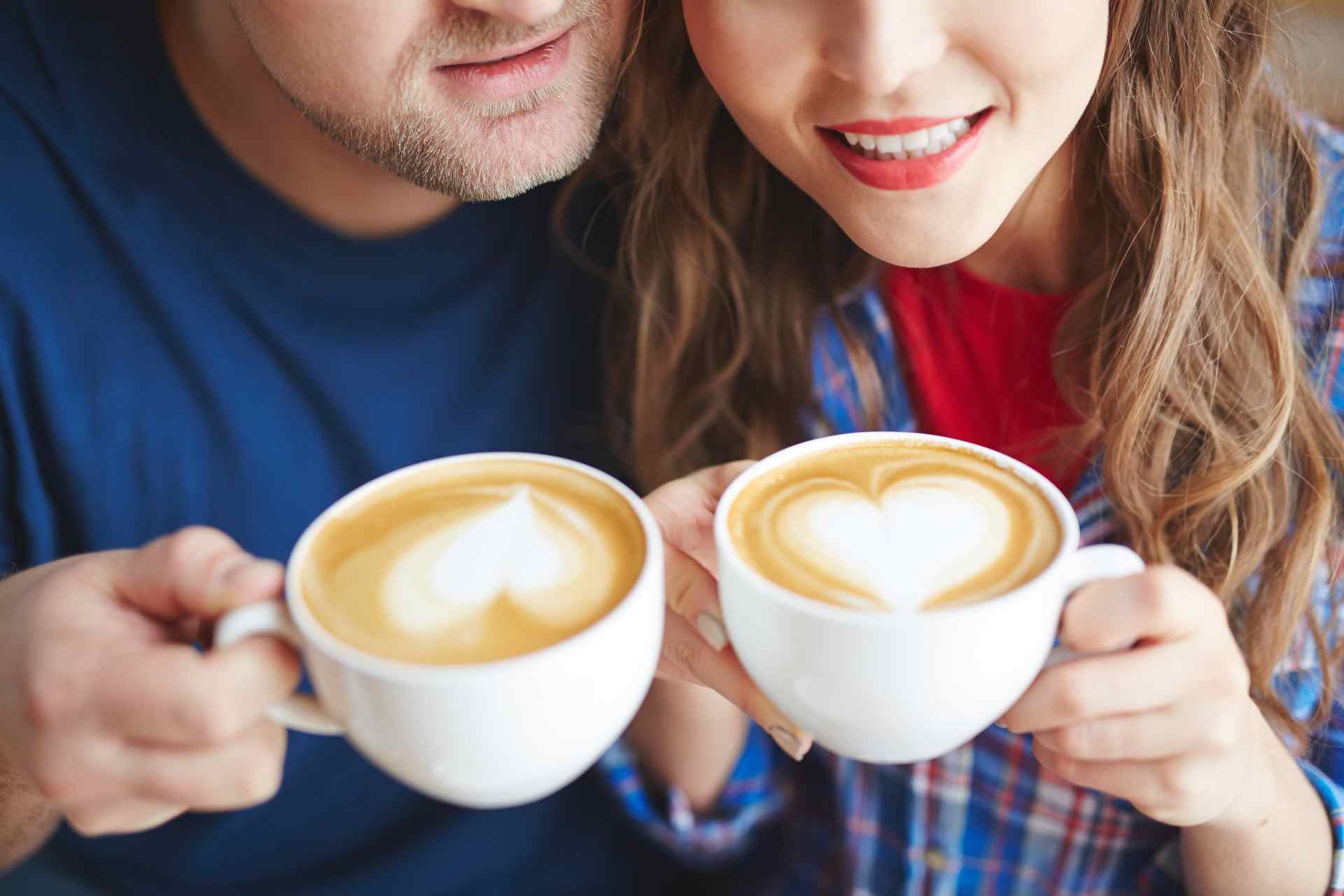 cute couple smiling over frothy latte coffee cups enjoying a casual firt date